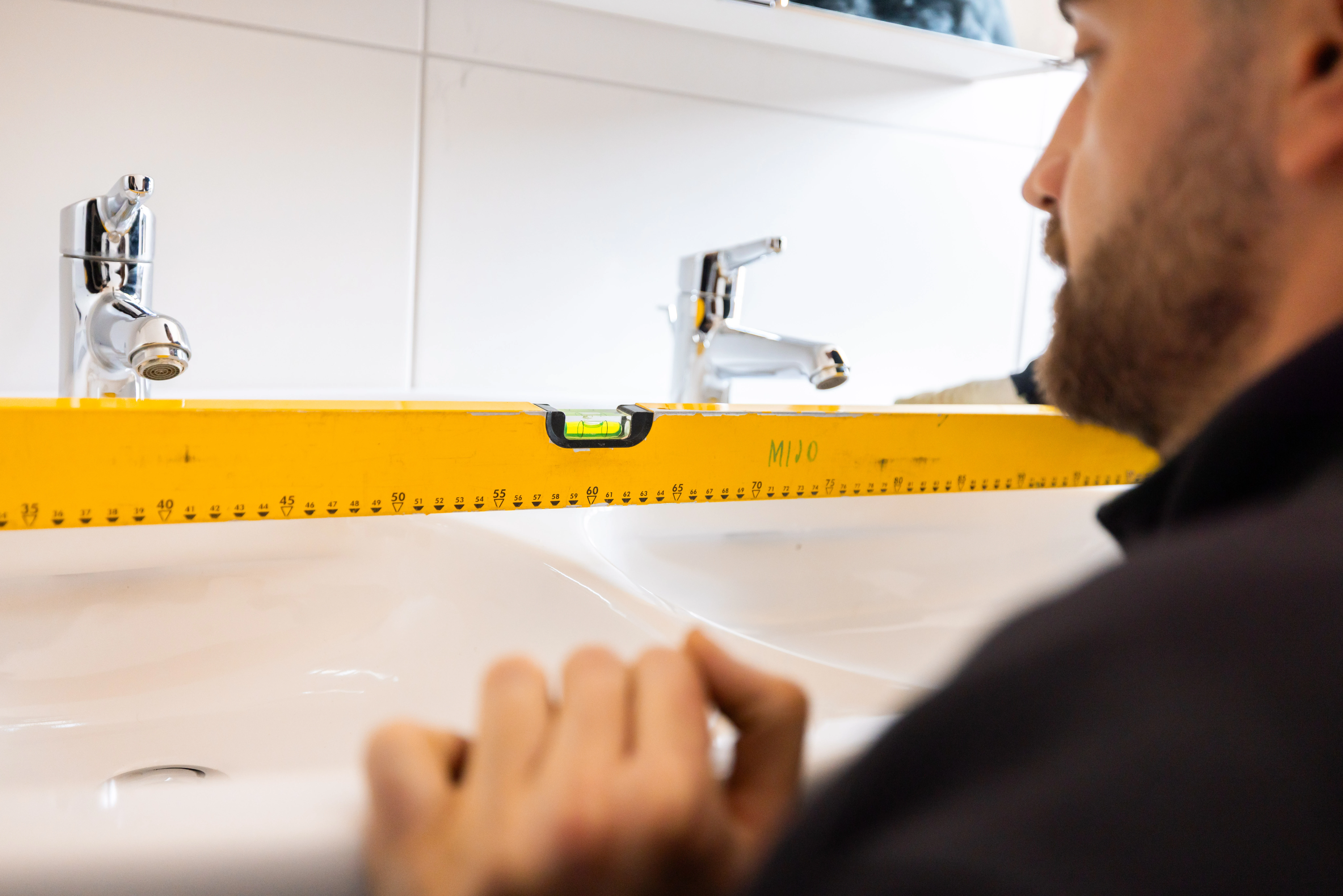 Sanitärinstallateur misst mit der Wasserwaage Waschtisch und Armaturen-Anschlüsse — Aufmass vor der Offerte